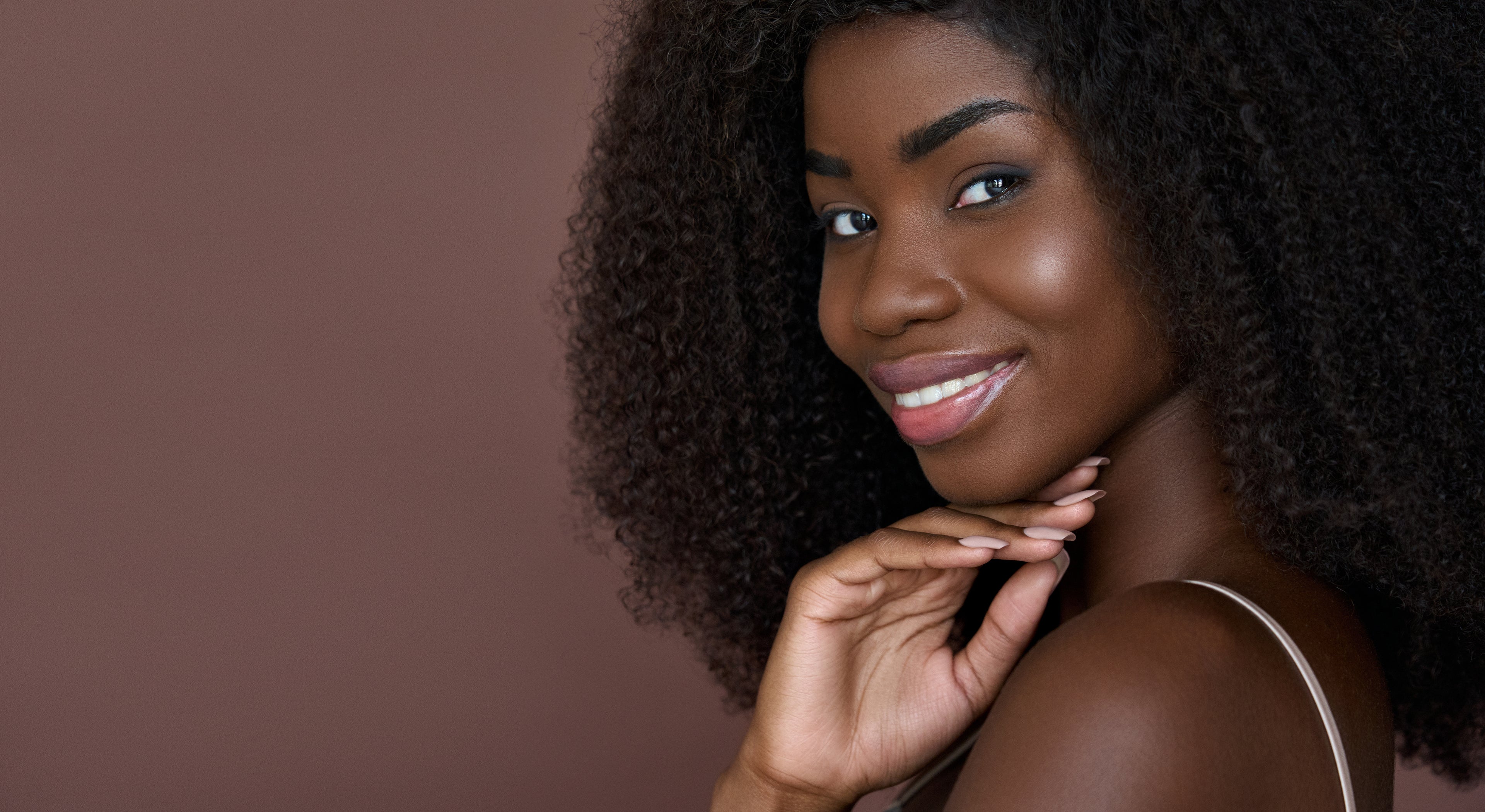 Woman with curly hair smiling against a brown background